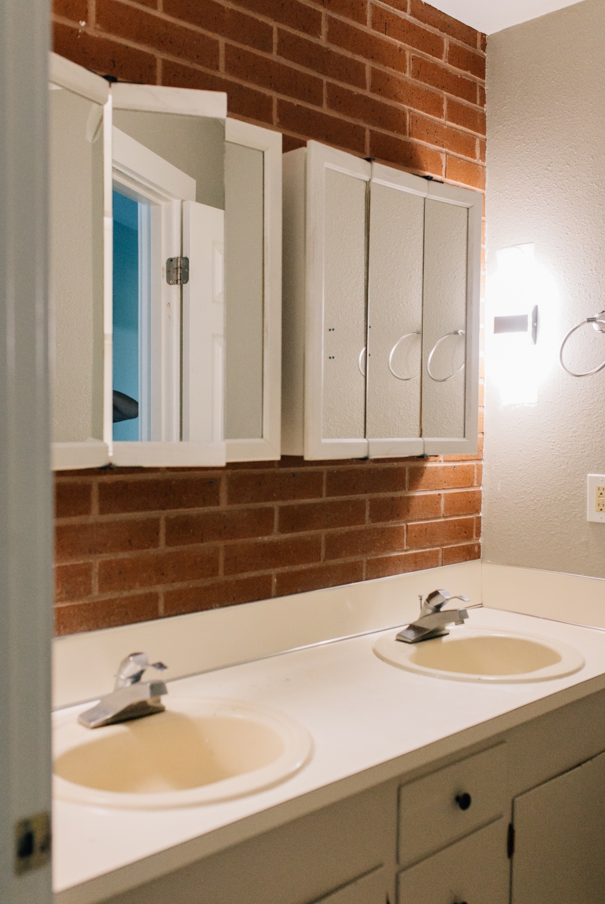 Bathroom with brick accent wall and dated double sink vanity